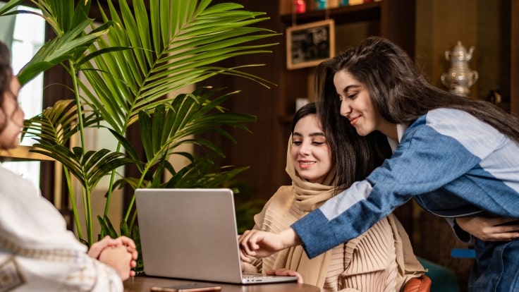 Arab girls are seen in a cafe, focused on a laptop submit their innovation for UAE’s Top Young Innovators